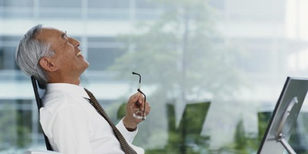 Mature businessman at desk by window, laughing, side view